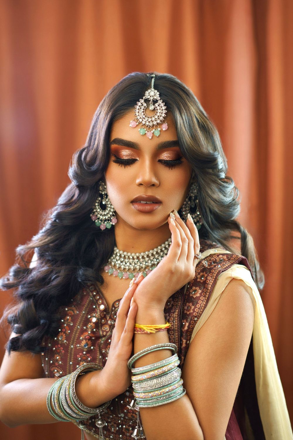 Portrait series showing elegant South Asian bridal jewelry and makeup with burgundy embellished attire against orange backdrop.