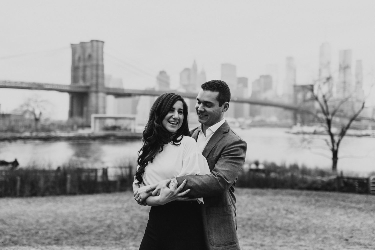 Romantic moment under the Brooklyn Bridge with Manhattan skyline in background.