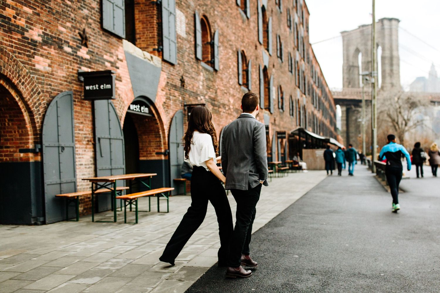 People walking along cobblestone street by historic brick buildings in DUMBO.