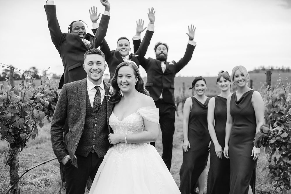 Wedding party jumps joyfully together in outdoor celebration photo.
