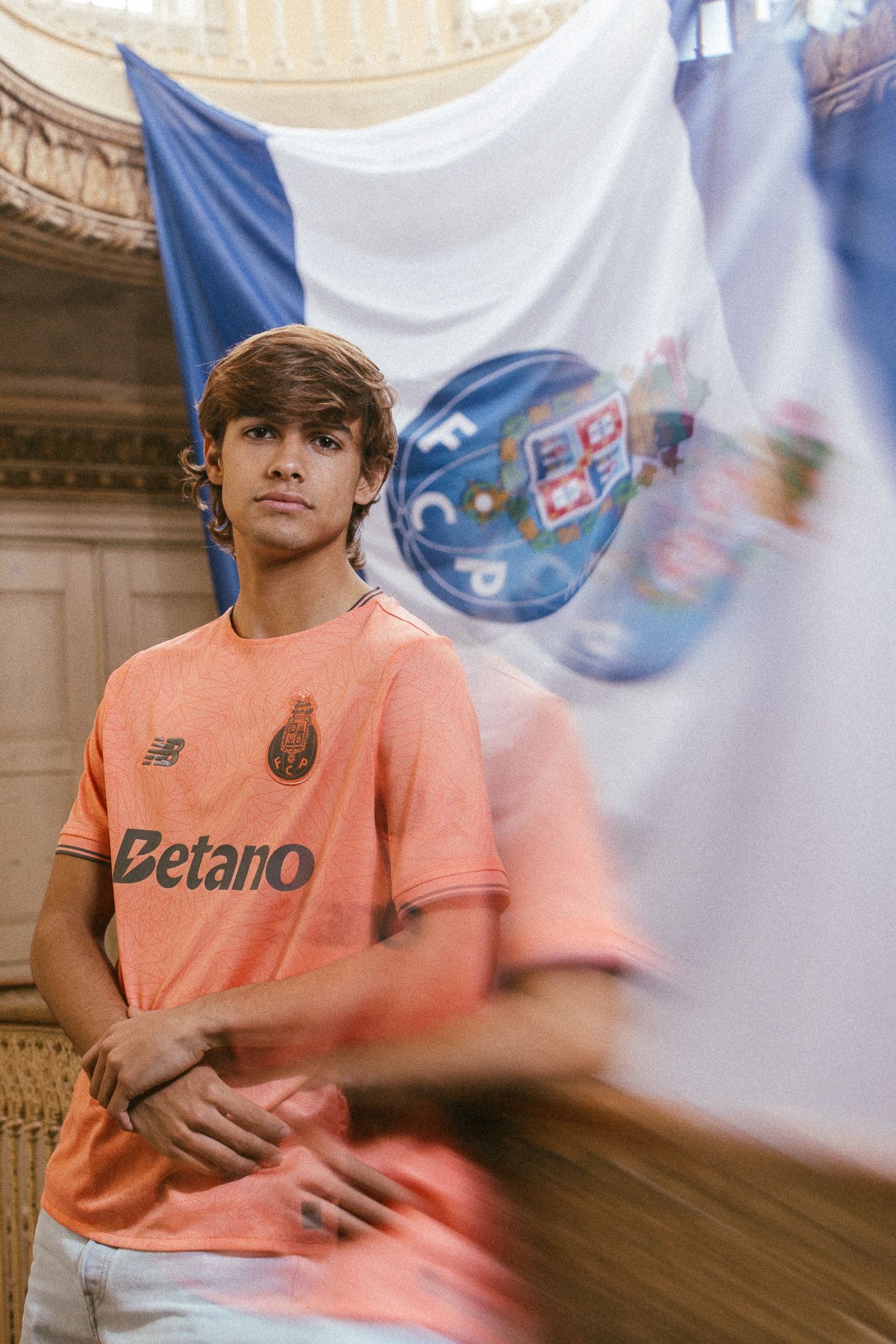 A person in a peach-colored Betano t-shirt poses in a motion-blurred sequence against an ornate architectural backdrop.