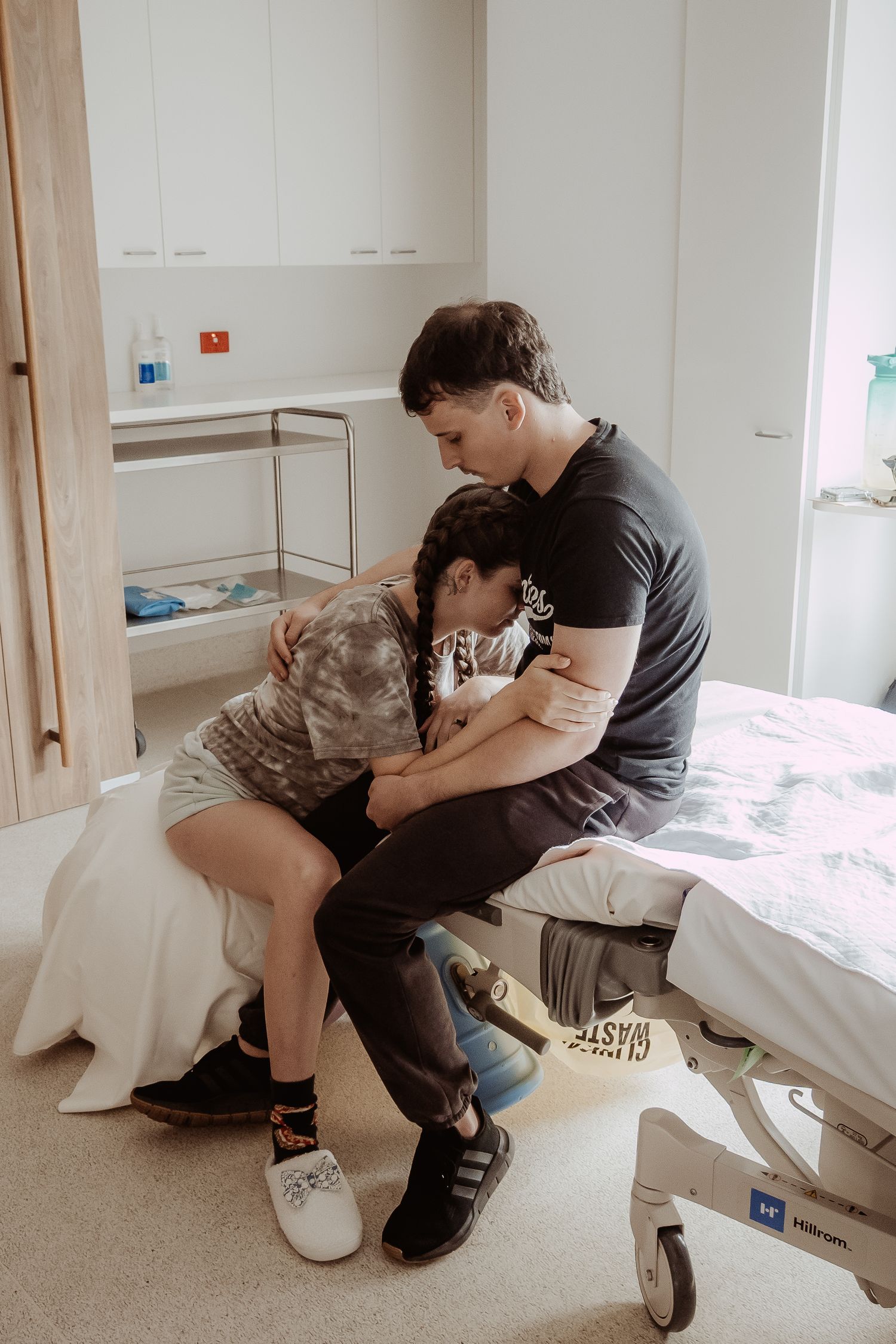 Tender moment shared between two people sitting on a hospital bed, offering comfort during a difficult time at a central coast birth session