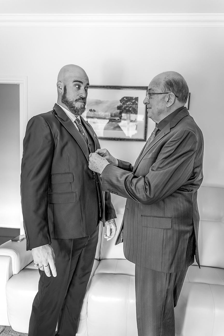 Two men in suits stand together as one adjusts the other's tie in a formal black and white photograph.
