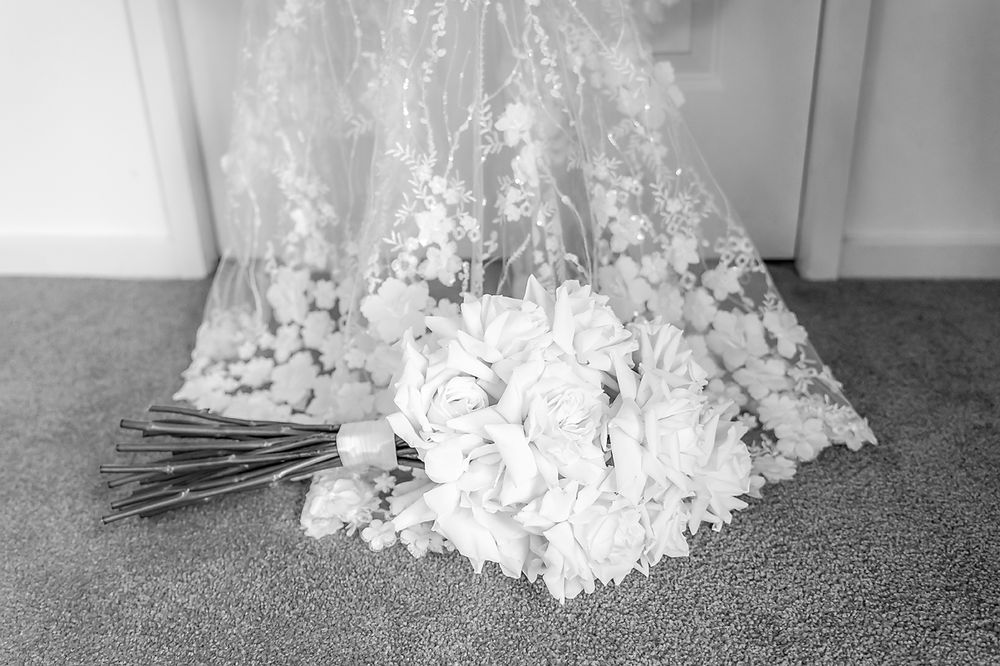 A delicate lace wedding veil and white rose bouquet lay on grey carpet in black and white photography.