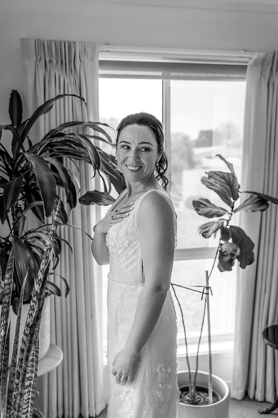 A sequence of black and white photos showing a bride in a white lace wedding dress standing near indoor plants and windows.