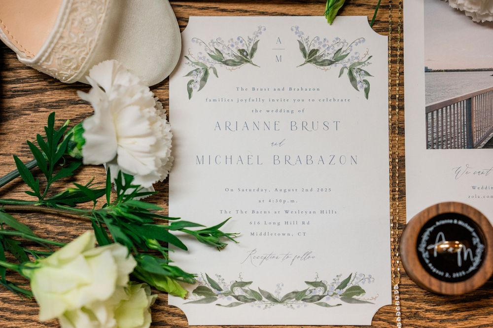 Elegant wedding invitation with green botanical design and white flowers on wooden surface.