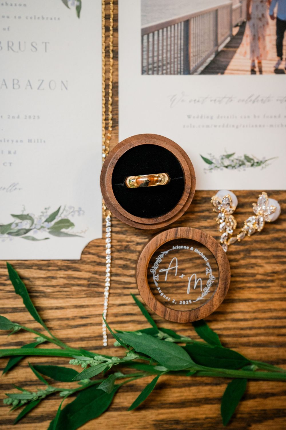 Wedding rings and jewelry displayed in wooden boxes with greenery accents on rustic wood surface.