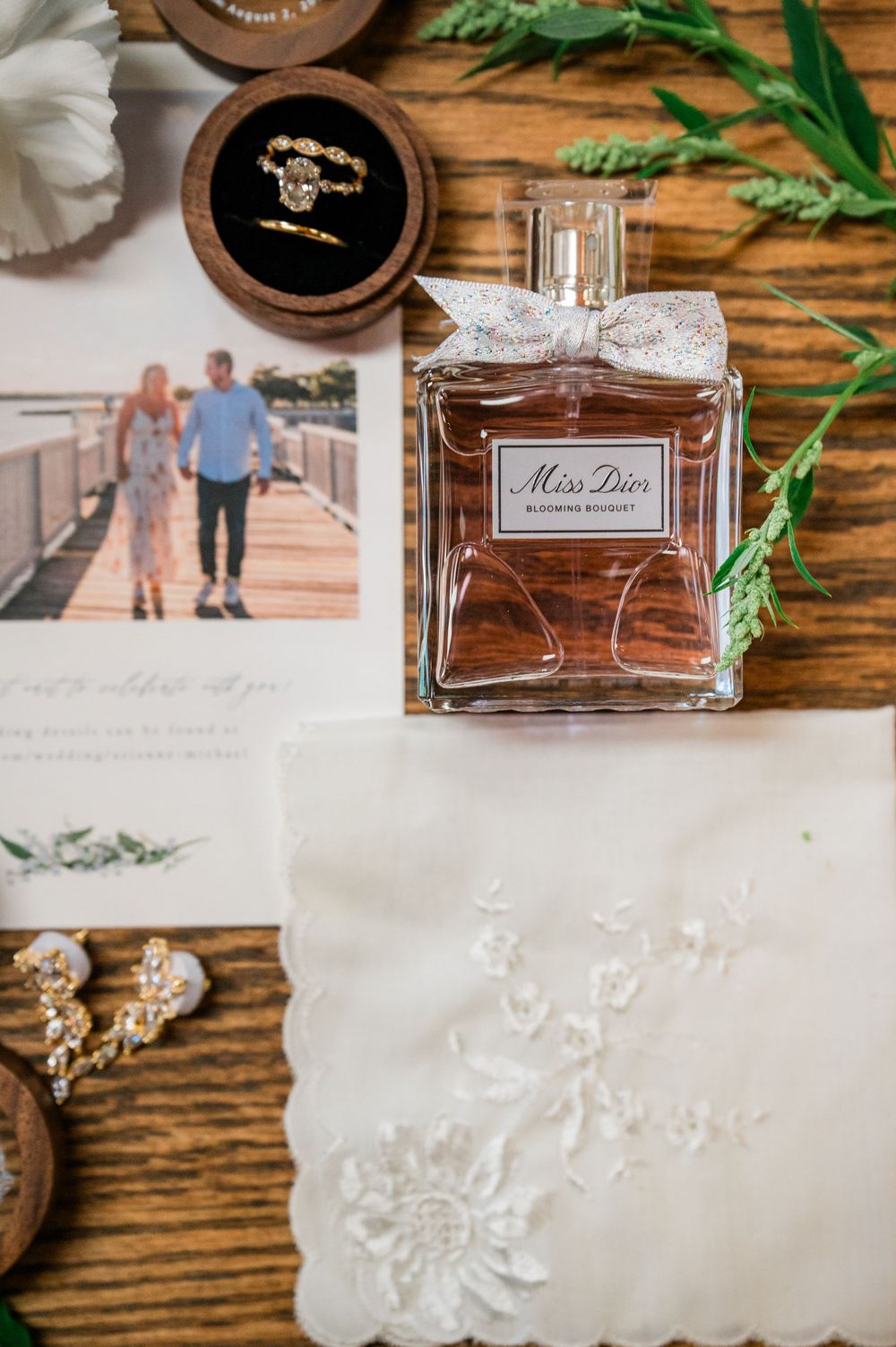 Miss Dior perfume bottle and wedding details arranged on rustic wooden surface with rings and lace accents.