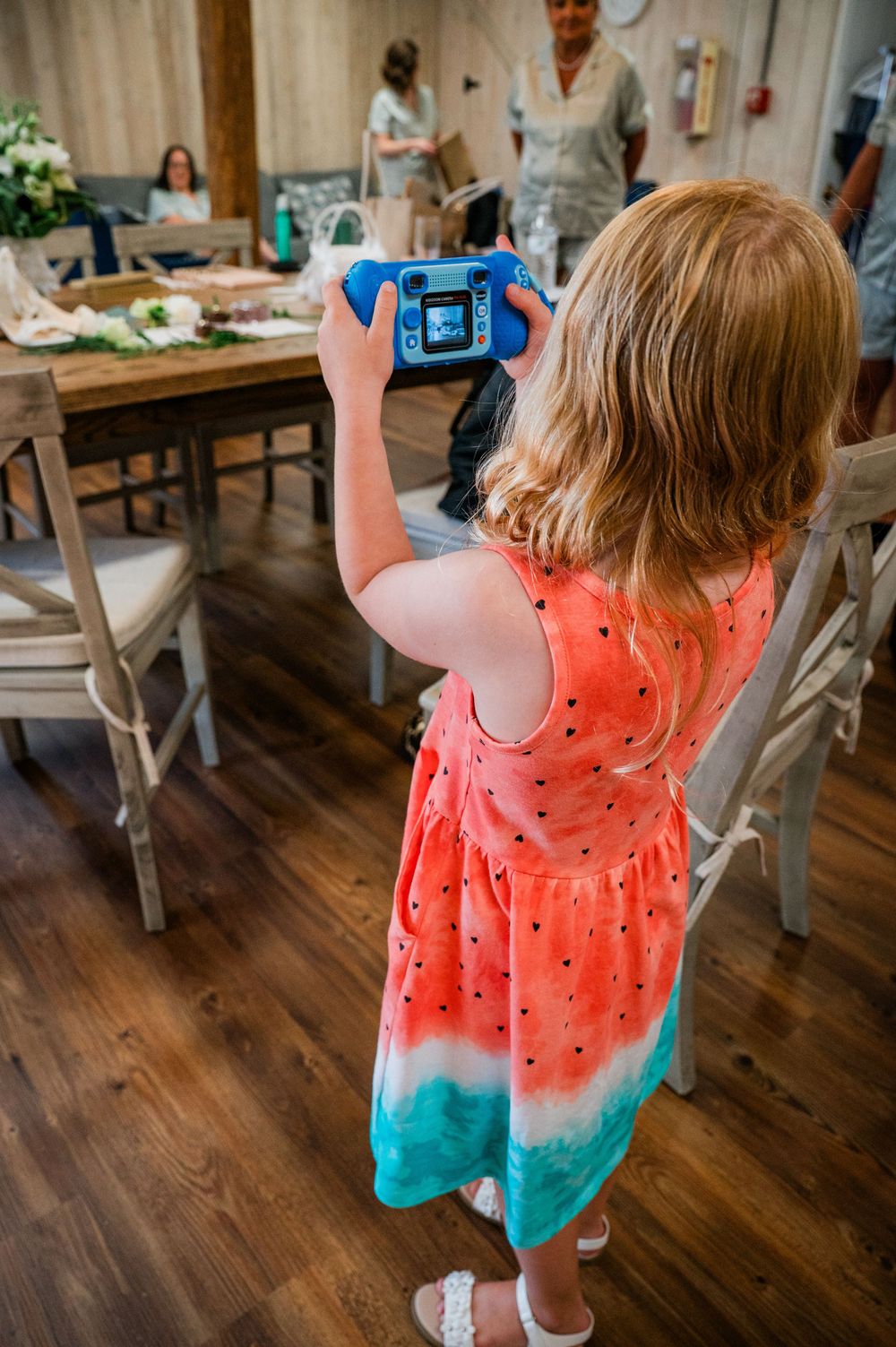 Young photographer in watermelon-print dress taking pictures at an indoor event.