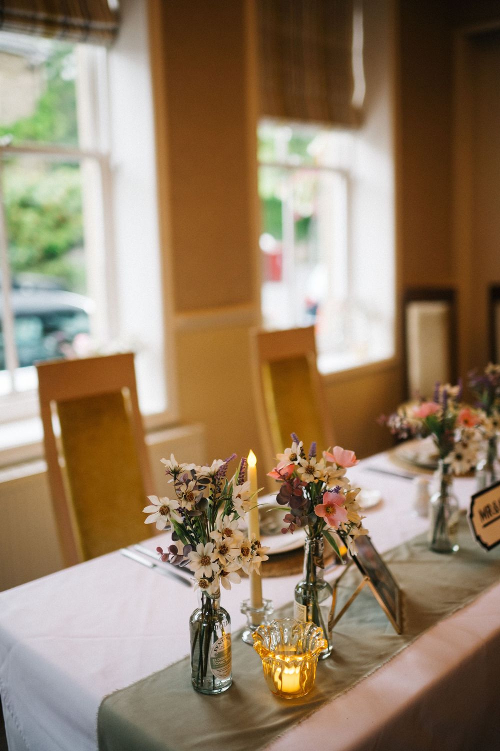 Wedding reception table decorated with rustic centerpieces featuring candles and wildflowers in mason jars.