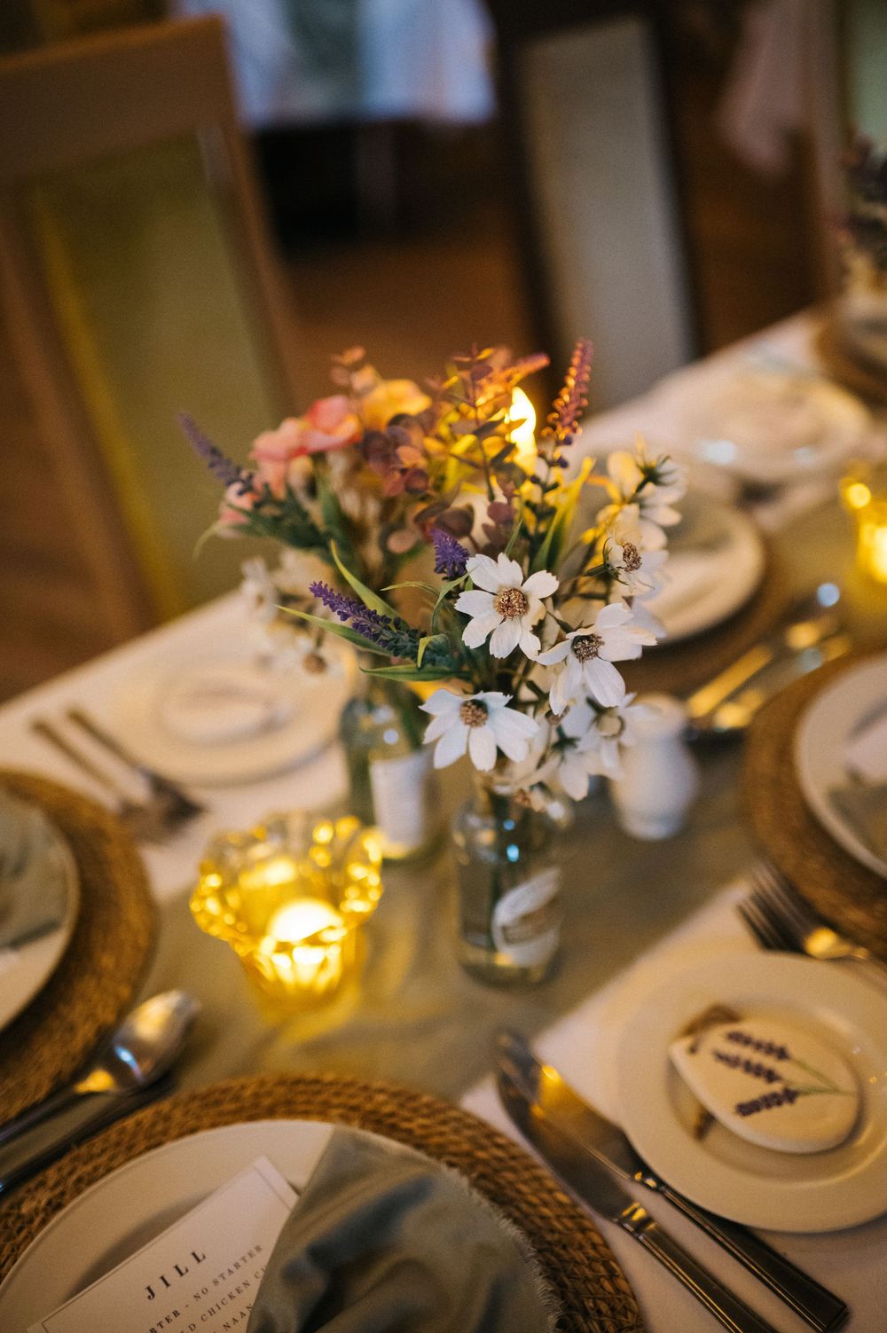 Intimate wedding table setting with floral centerpiece and glowing candles on white linens.