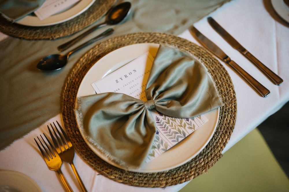 Elegant place settings with gold chargers and sage green napkins at a wedding reception.