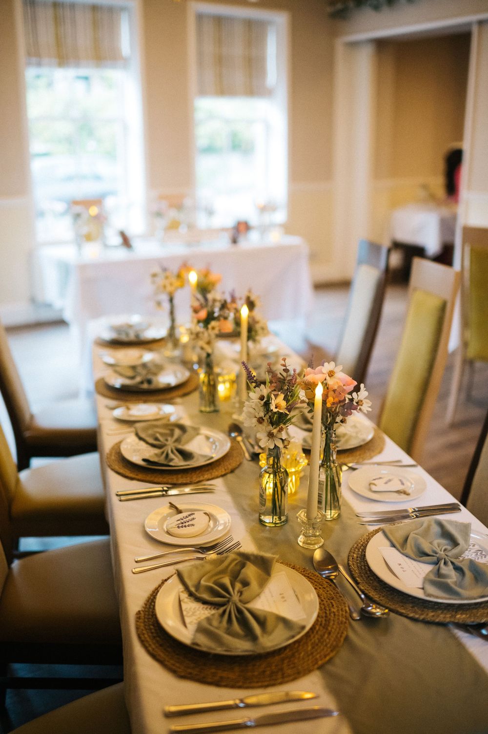Elegant wedding table setting with gold chargers, candles, and floral centerpieces in a bright dining room.