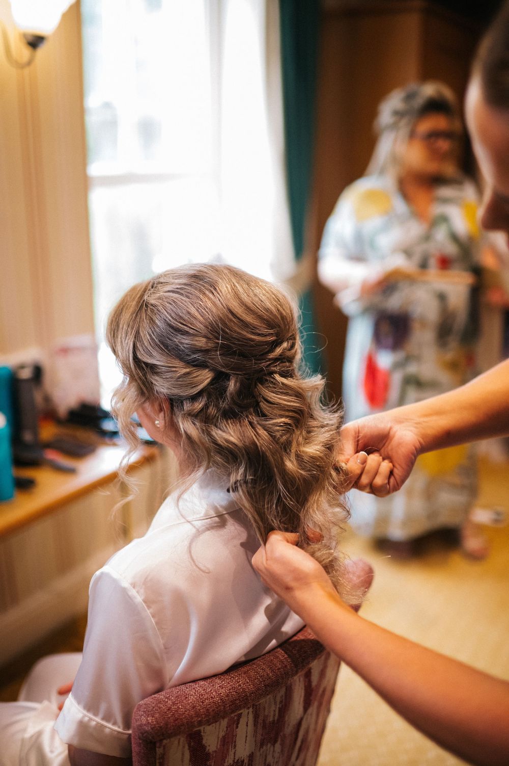 Hair styling session in progress with white robes and natural lighting in a preparation room.