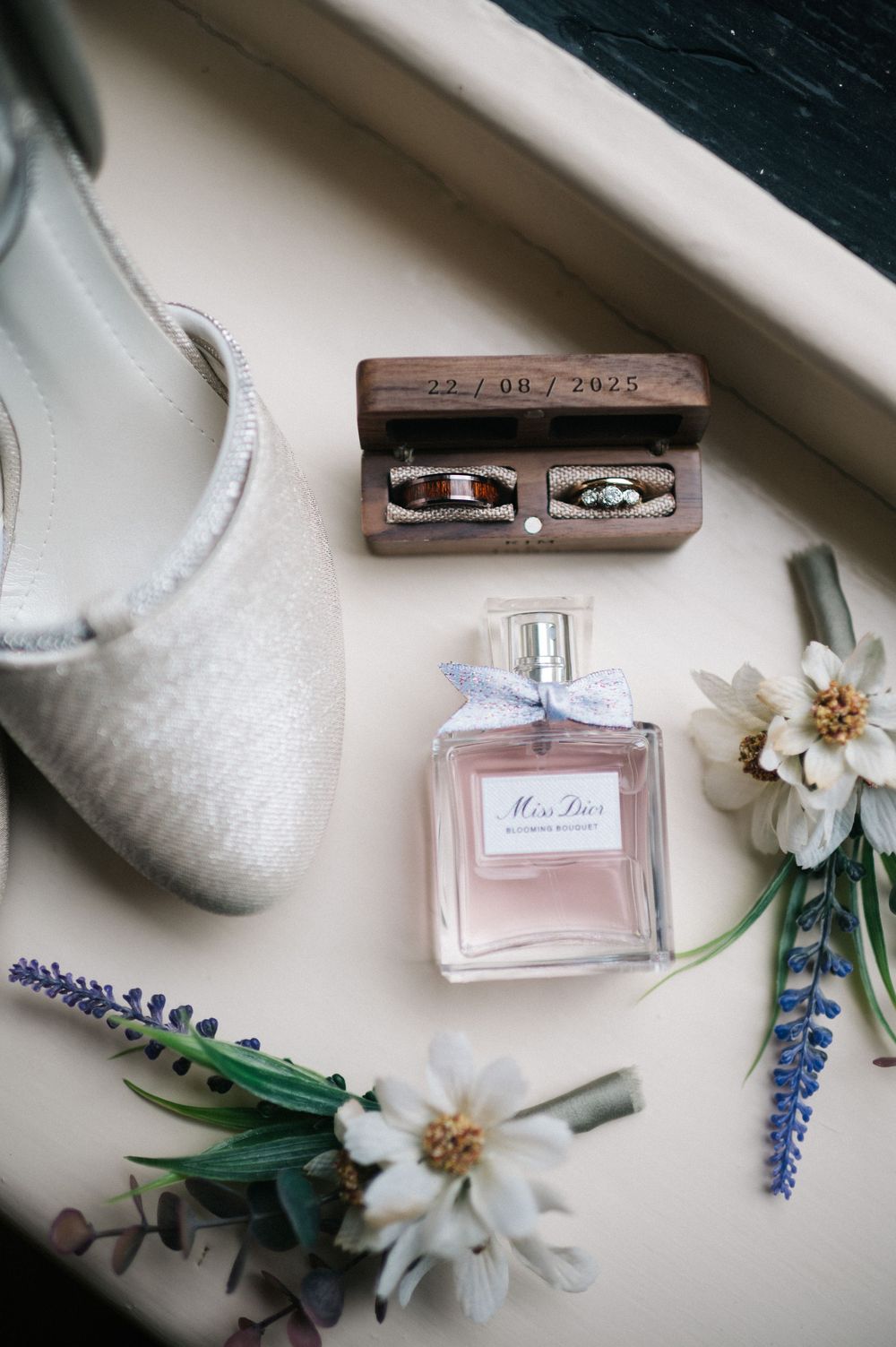 Wedding details with perfume bottle, white flowers, and lavender sprigs arranged on a light surface.