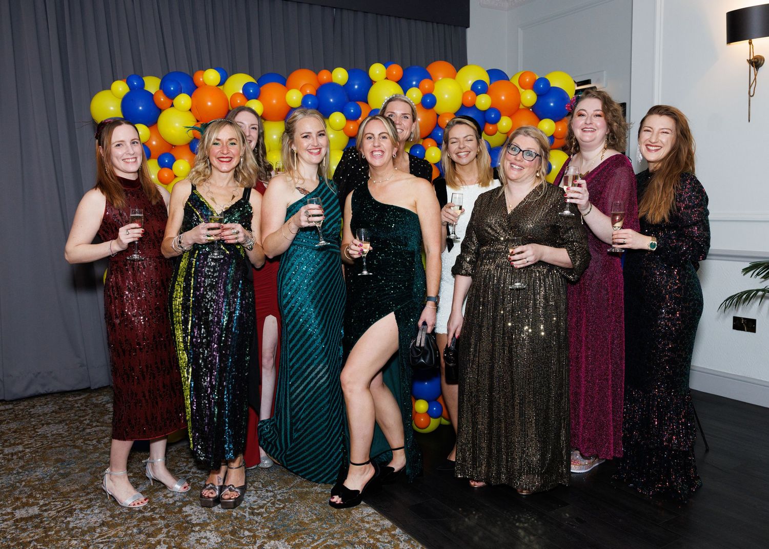 Group of party guests in formal attire dancing and celebrating with colorful balloons decorating the venue.