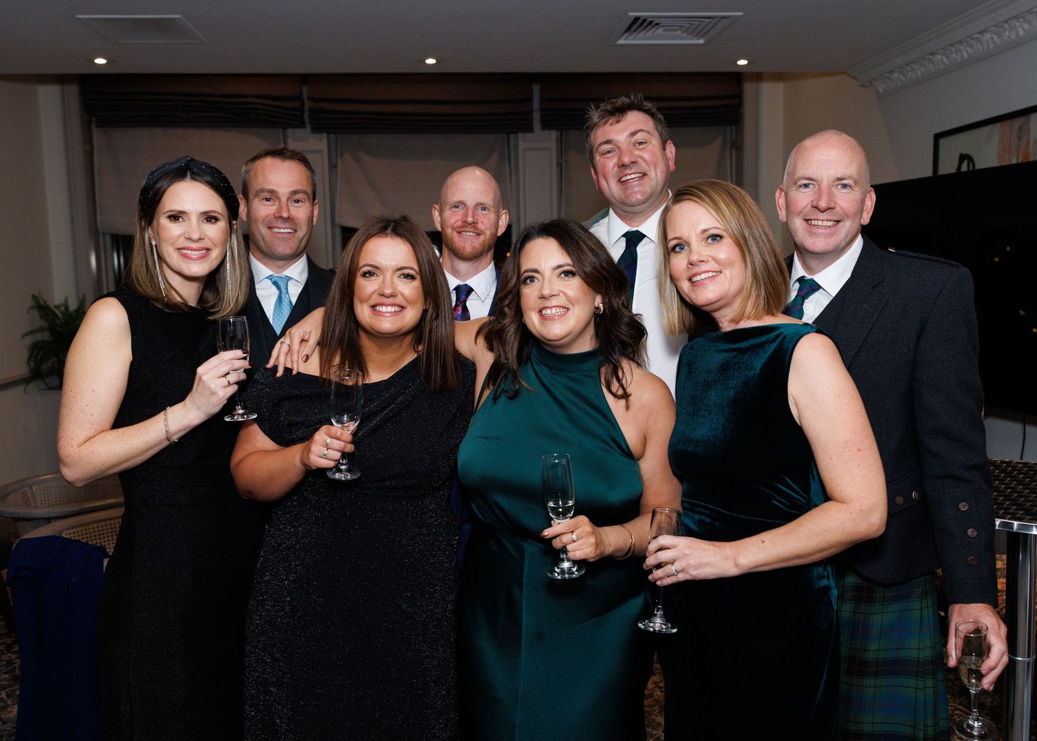 A group of people in formal attire smile and pose together at an evening social event.