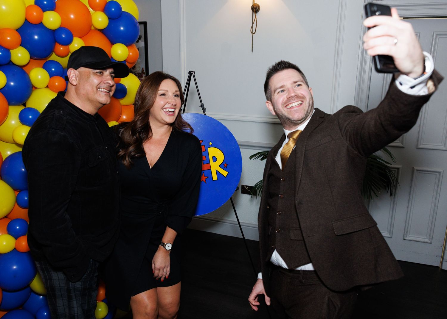 A group of people dancing and celebrating at a party with colorful blue and yellow balloons in the background.