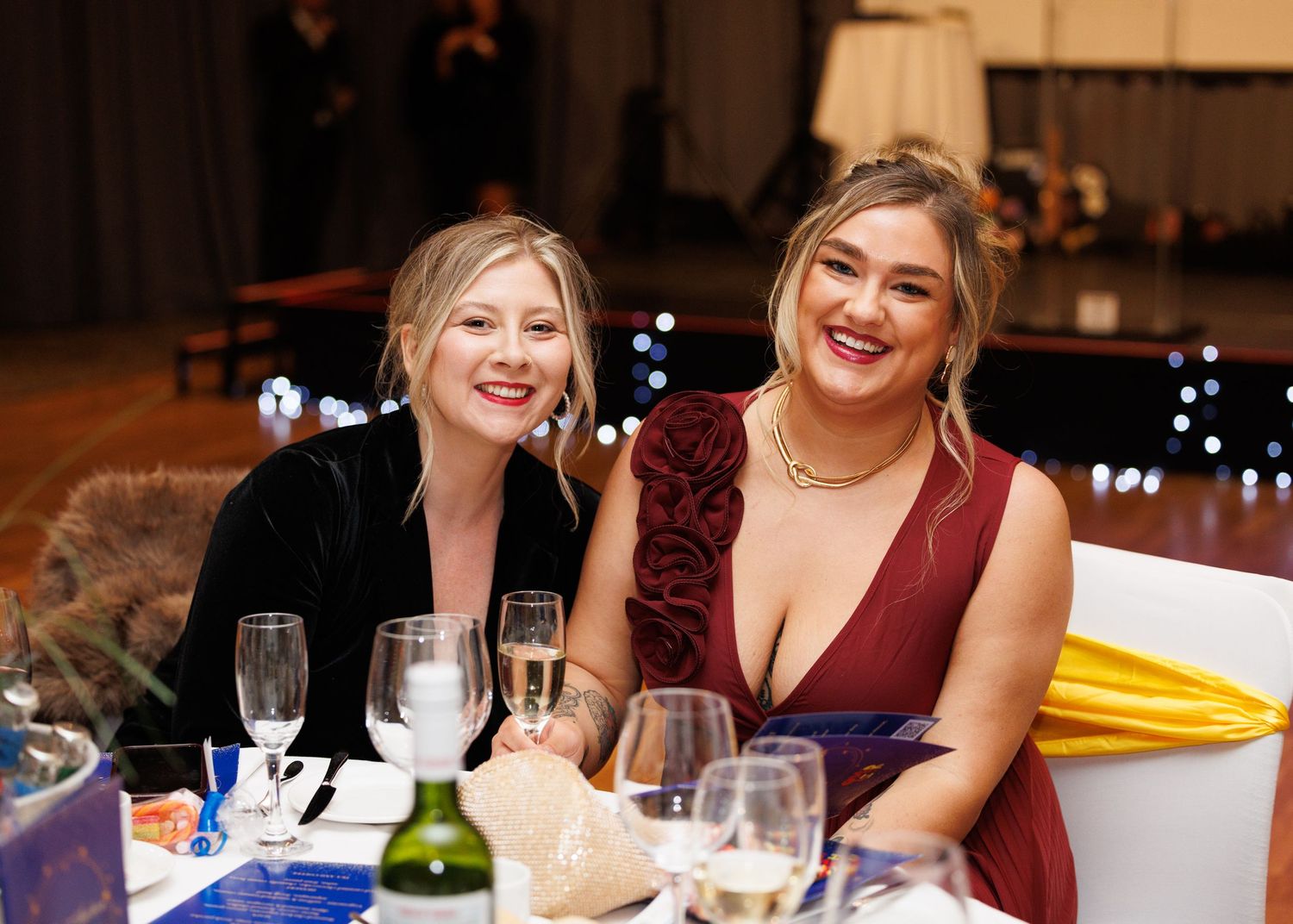 Wedding guests in burgundy dresses enjoy dinner and conversation at an elegant evening reception.