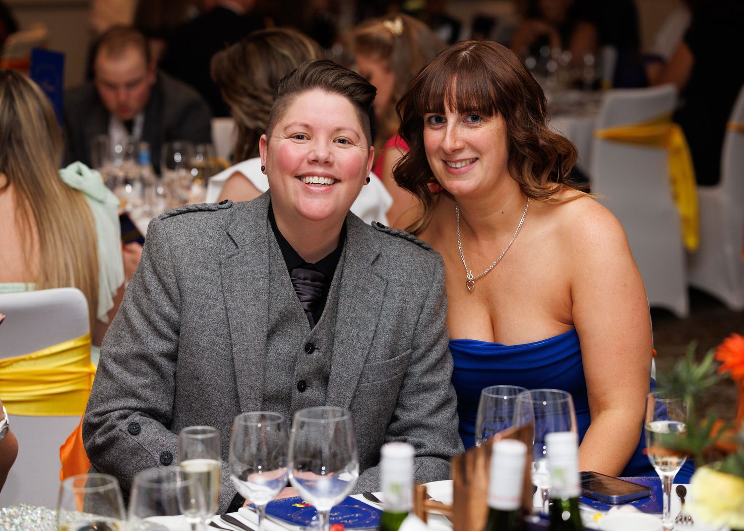 Two guests enjoying themselves at a formal dinner event with wine glasses and table settings visible.