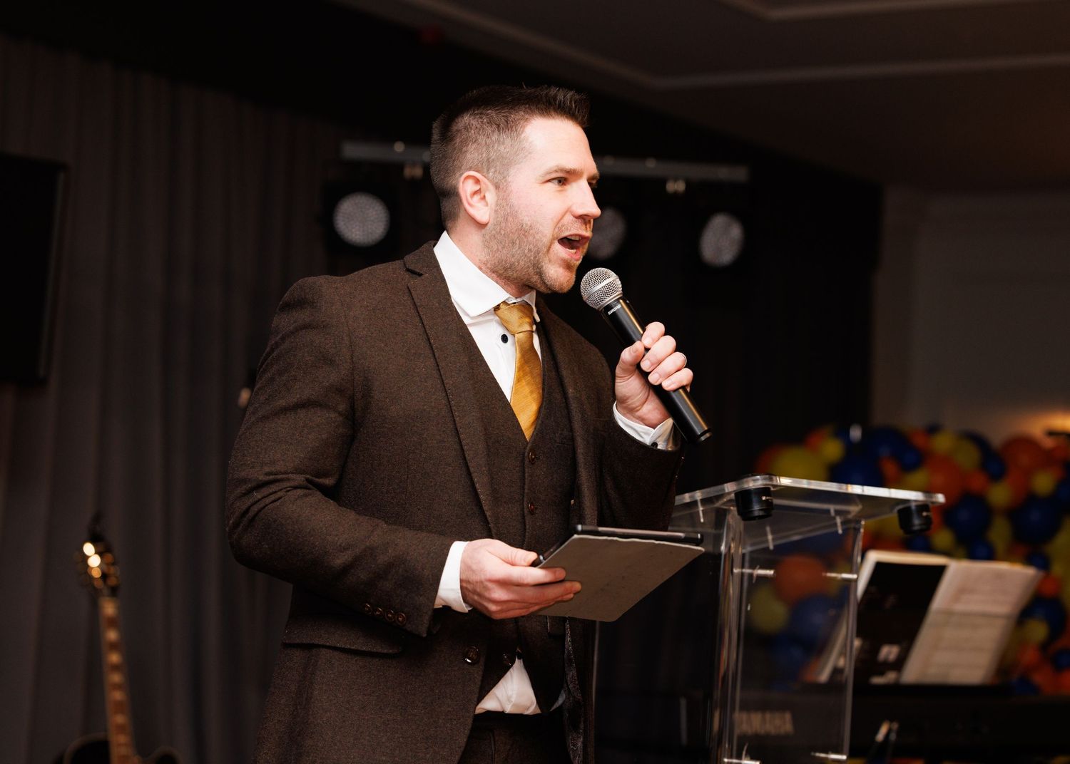 Professional singer performs at an event wearing a brown suit and orange tie while holding a microphone.