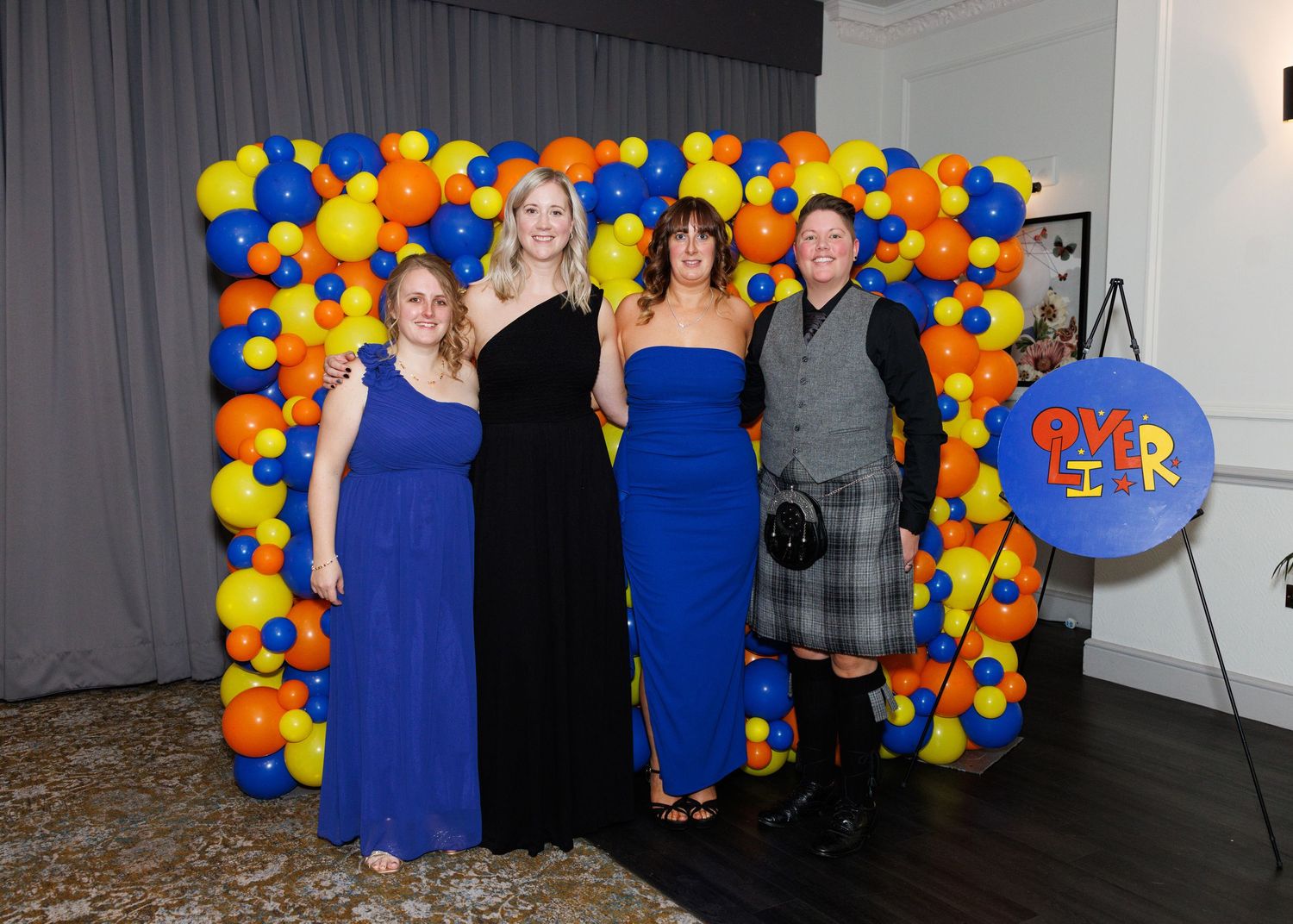 People pose in front of a colorful balloon arch display at a formal event.