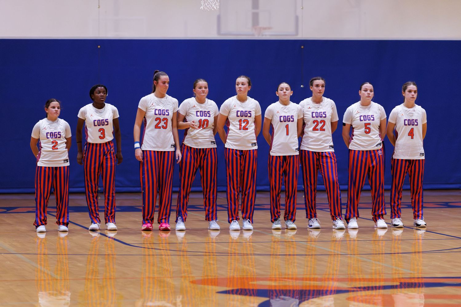 Basketball team lines up on court wearing white uniforms during pre-game ceremony.