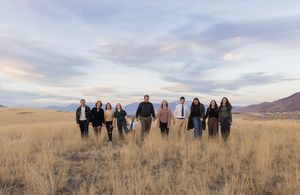 Extended family walking hand in hand through an open field at sunset during a Utah family session