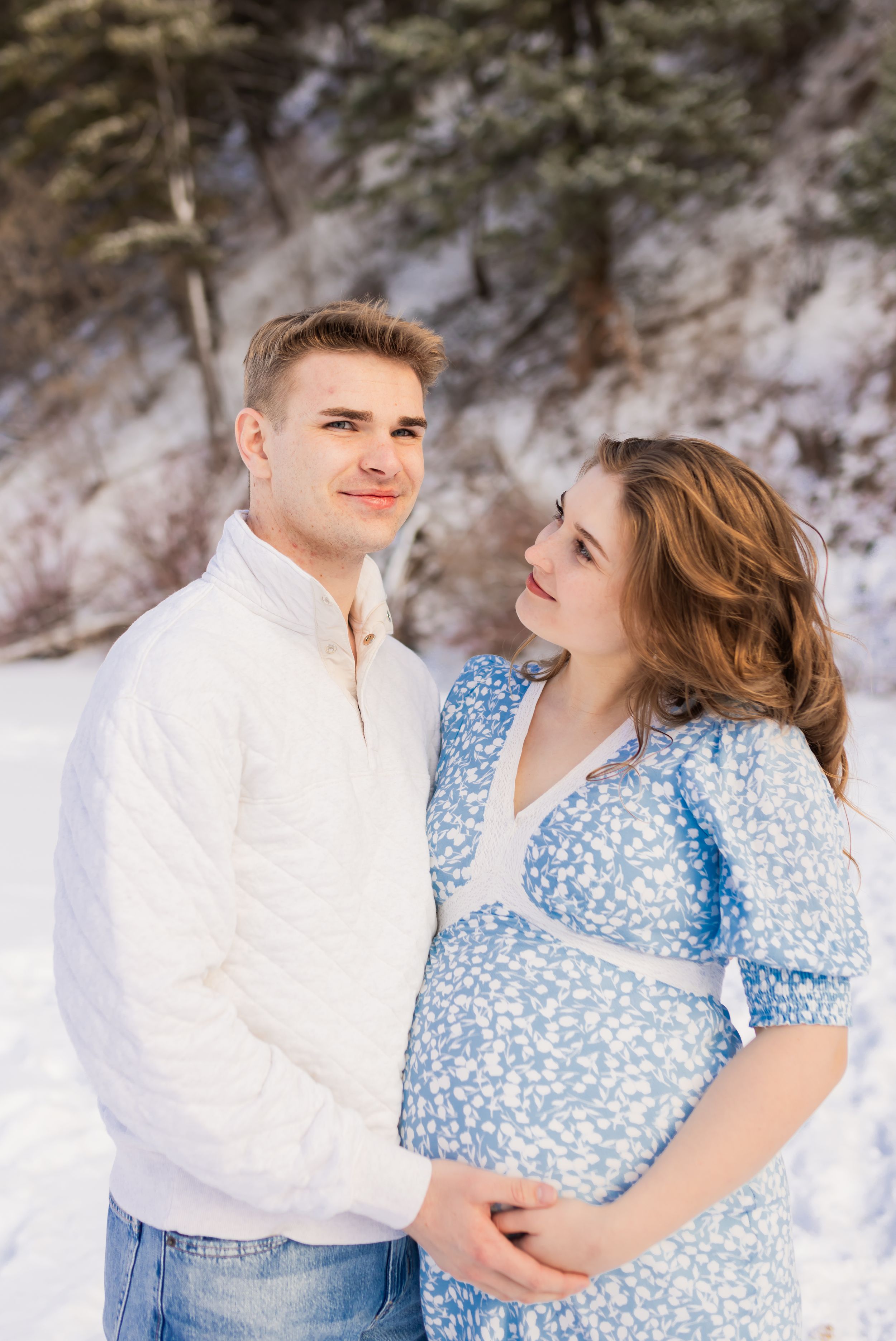 Utah maternity session of expecting couple smiling together in a snowy mountain setting