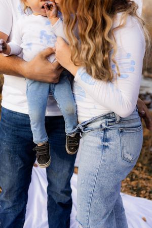 Lifestyle family photography detail of parents holding toddler, candid moment with paint-covered hands