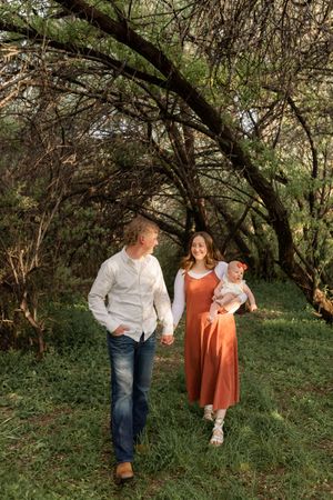 Parents holding their baby while walking through a wooded trail during a Utah family photography session
