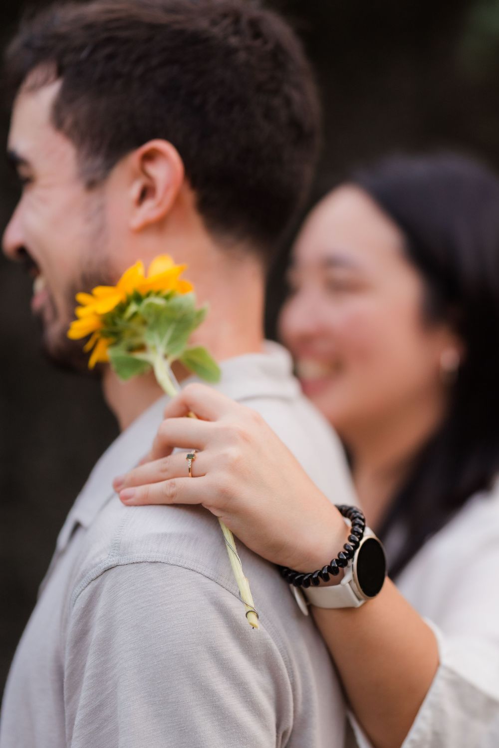 A sunflower is held between two people wearing light colored clothing in a tender moment.