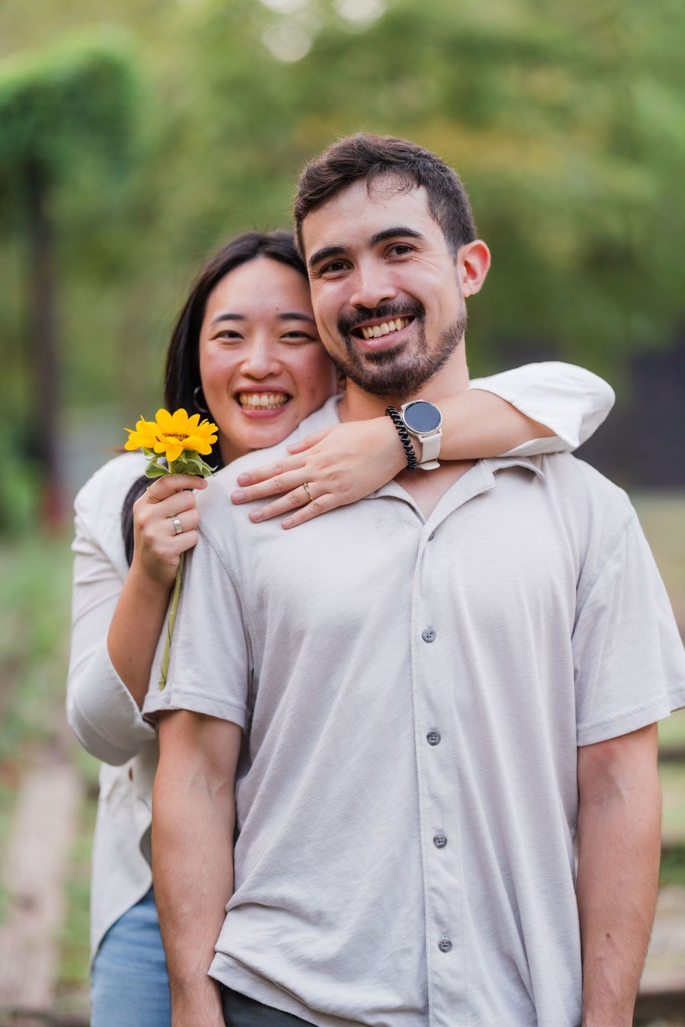 A couple shares joyful laughter and embraces while wearing white shirts in a sunny outdoor setting.