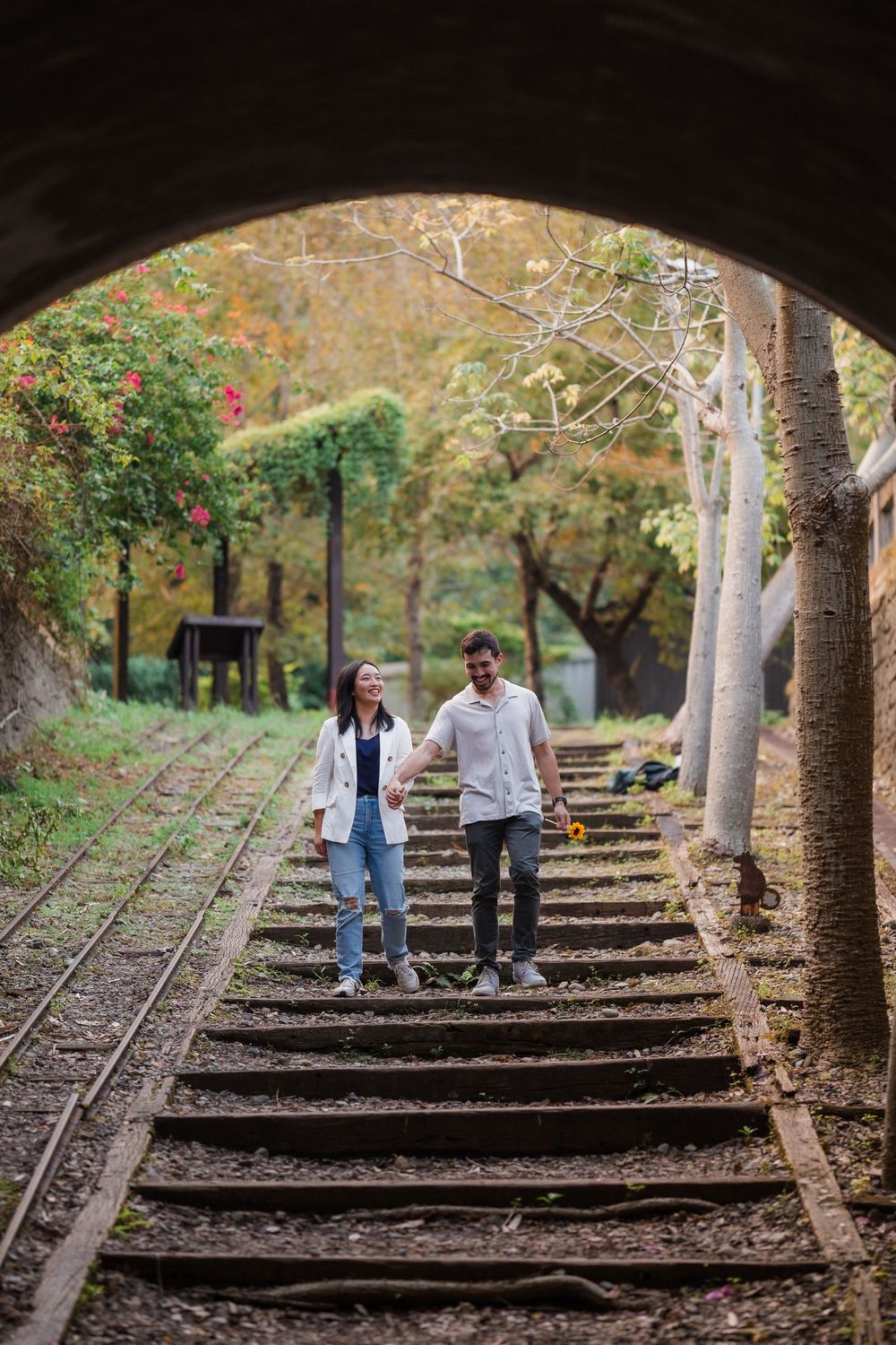 Couple walking up rustic wooden steps through a tunnel surrounded by autumn foliage.