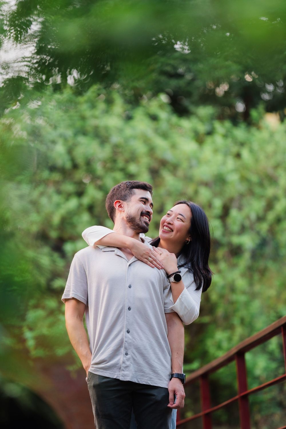 Happy couple laughing together in casual attire against a lush green background.
