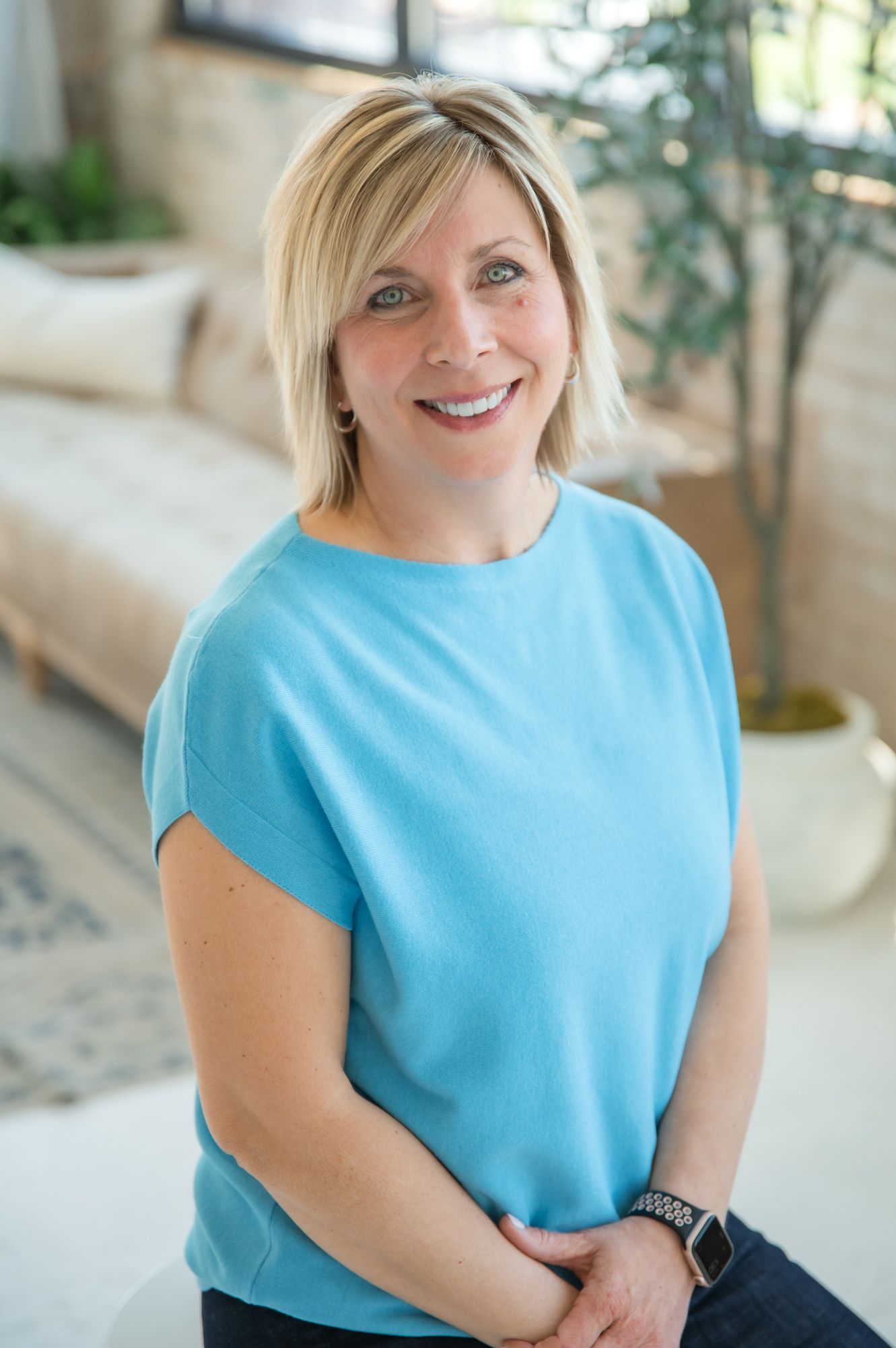 Professional headshot of a person wearing a light blue top in a bright indoor setting.