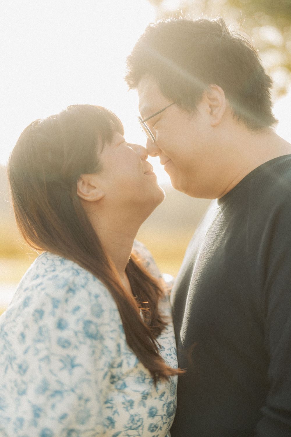 Couple sharing intimate moments in soft sunlit outdoor setting.