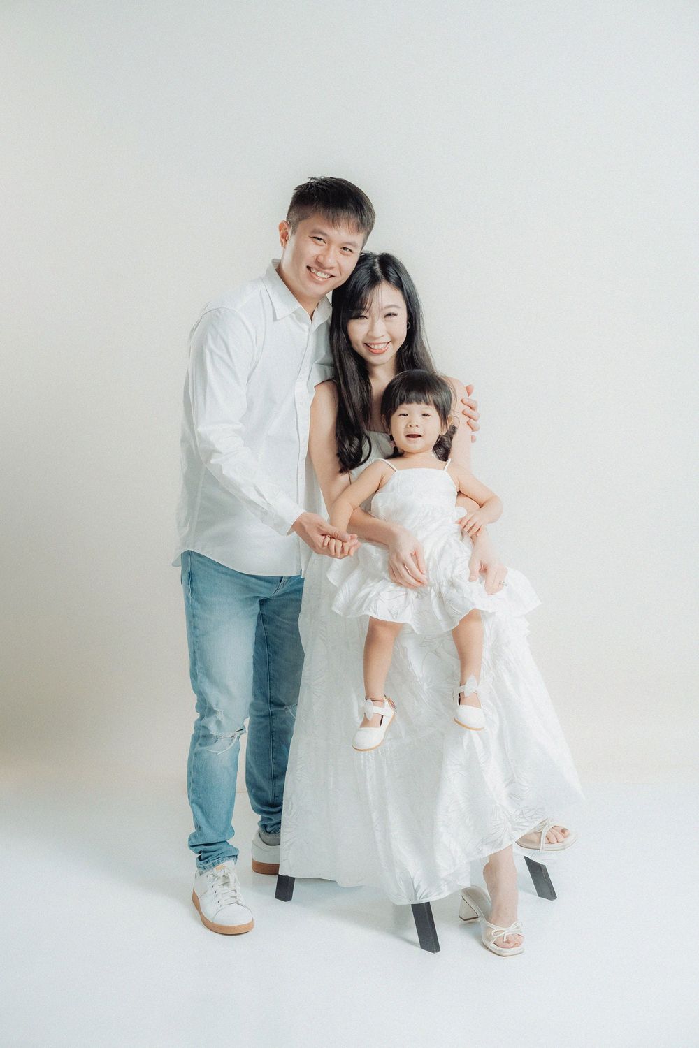 A family in matching white outfits poses playfully together against a bright studio backdrop.