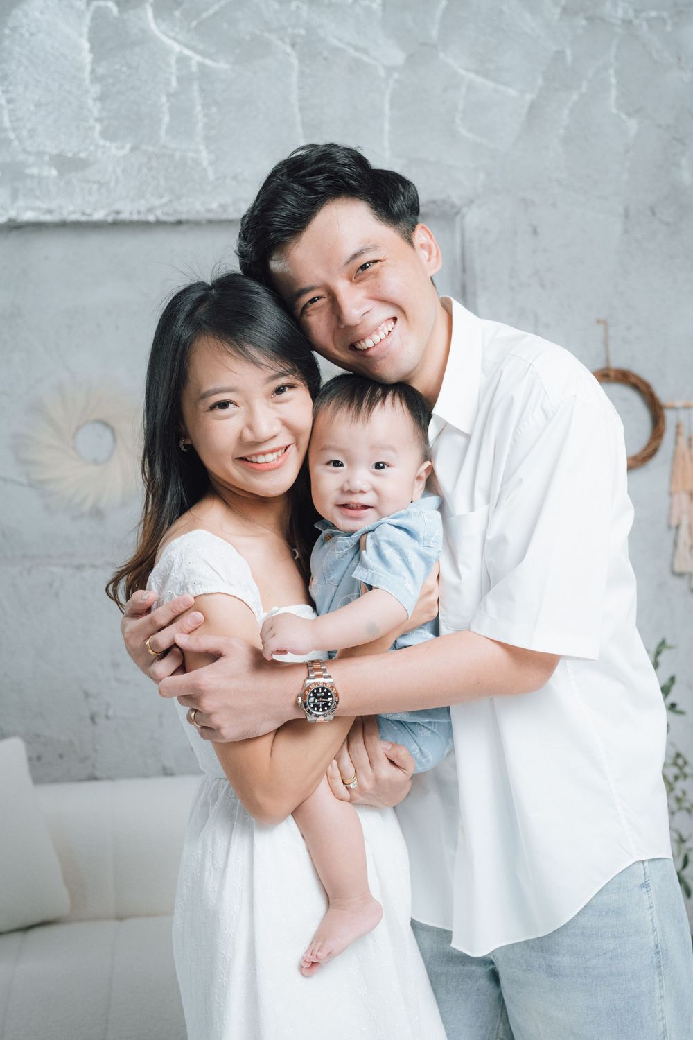 Family in white outfits posing against a grey wall in a studio setting.