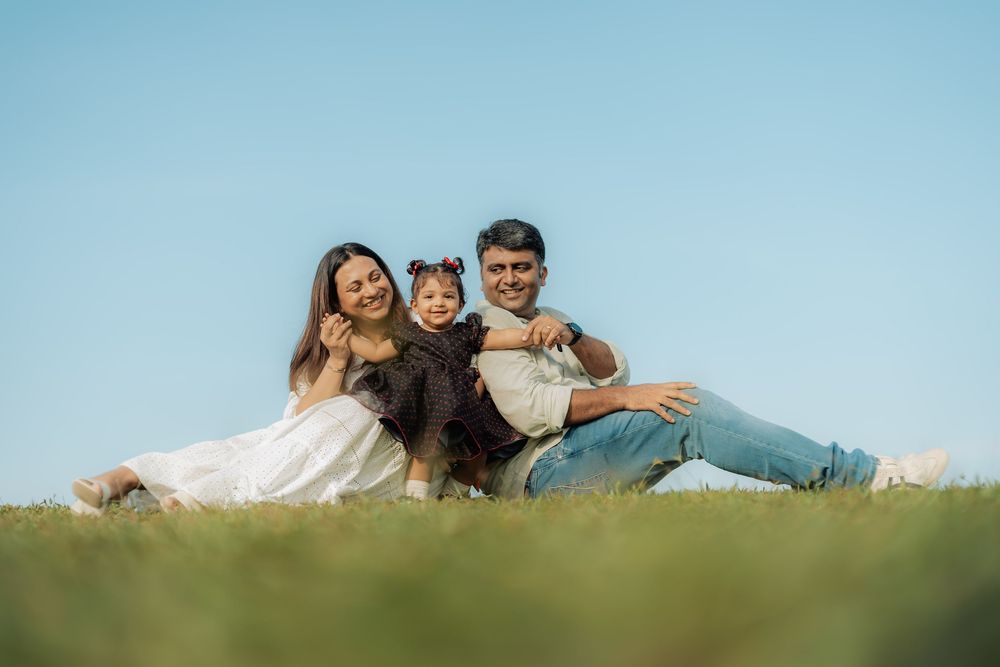 Family lying together on grassy hill against bright blue sky.