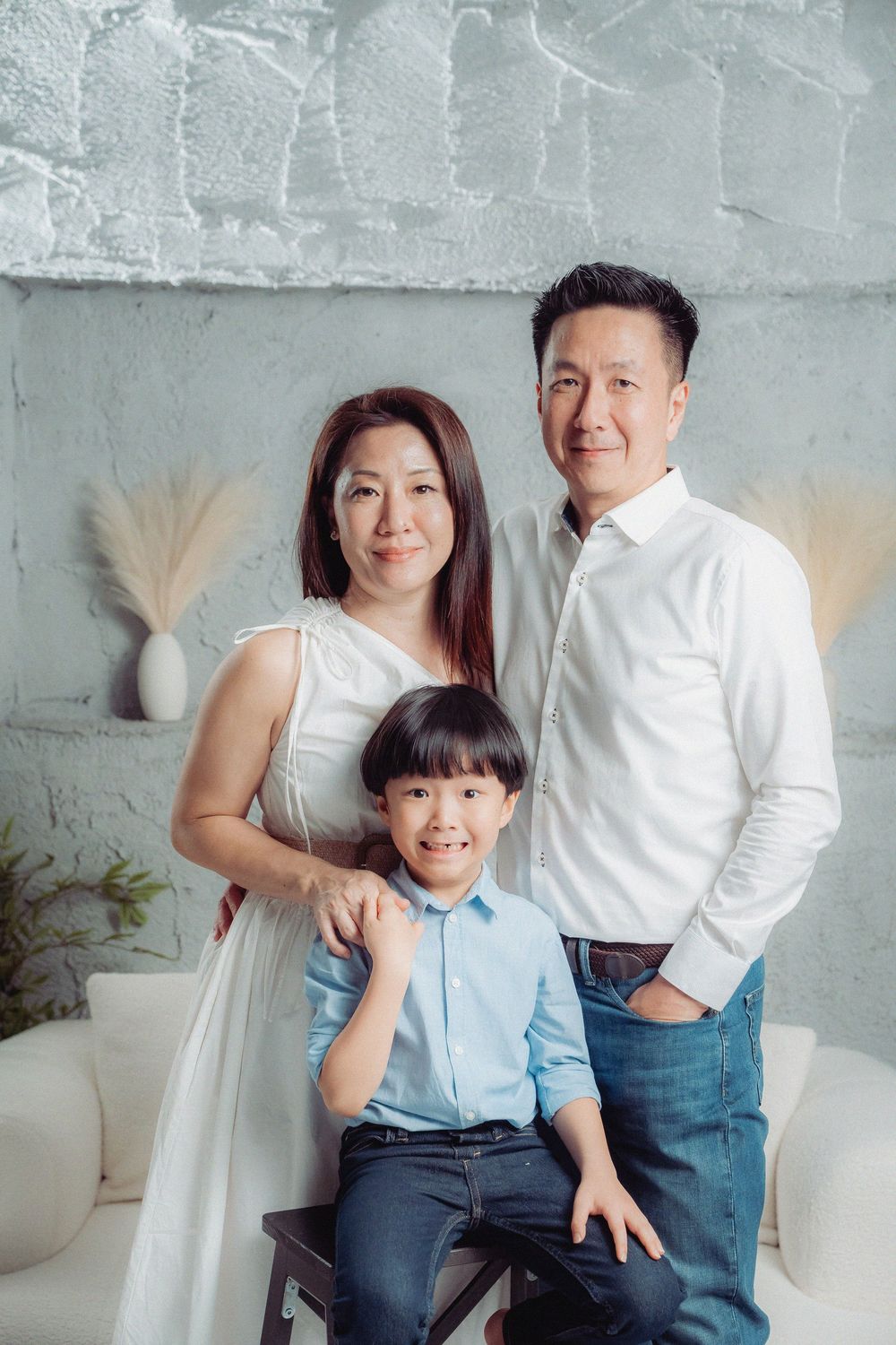 A family poses together against a textured gray wall with pampas grass decor in a modern studio setting.