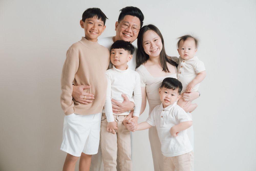 Family group portrait in coordinated neutral colored outfits against white background.