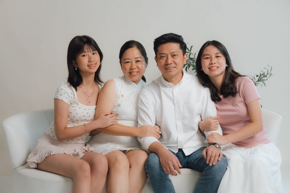 Family group sitting close together on couch in casual attire.