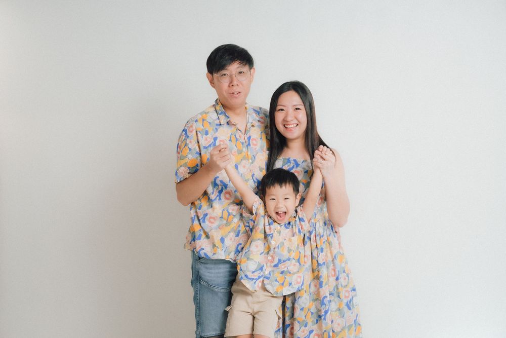 Family portrait with coordinated floral print outfits against white wall.