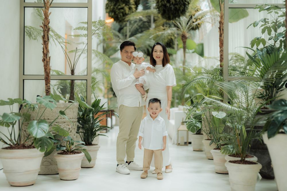 A series of four photos showing a family in white outfits walking through a bright indoor space filled with potted plants.