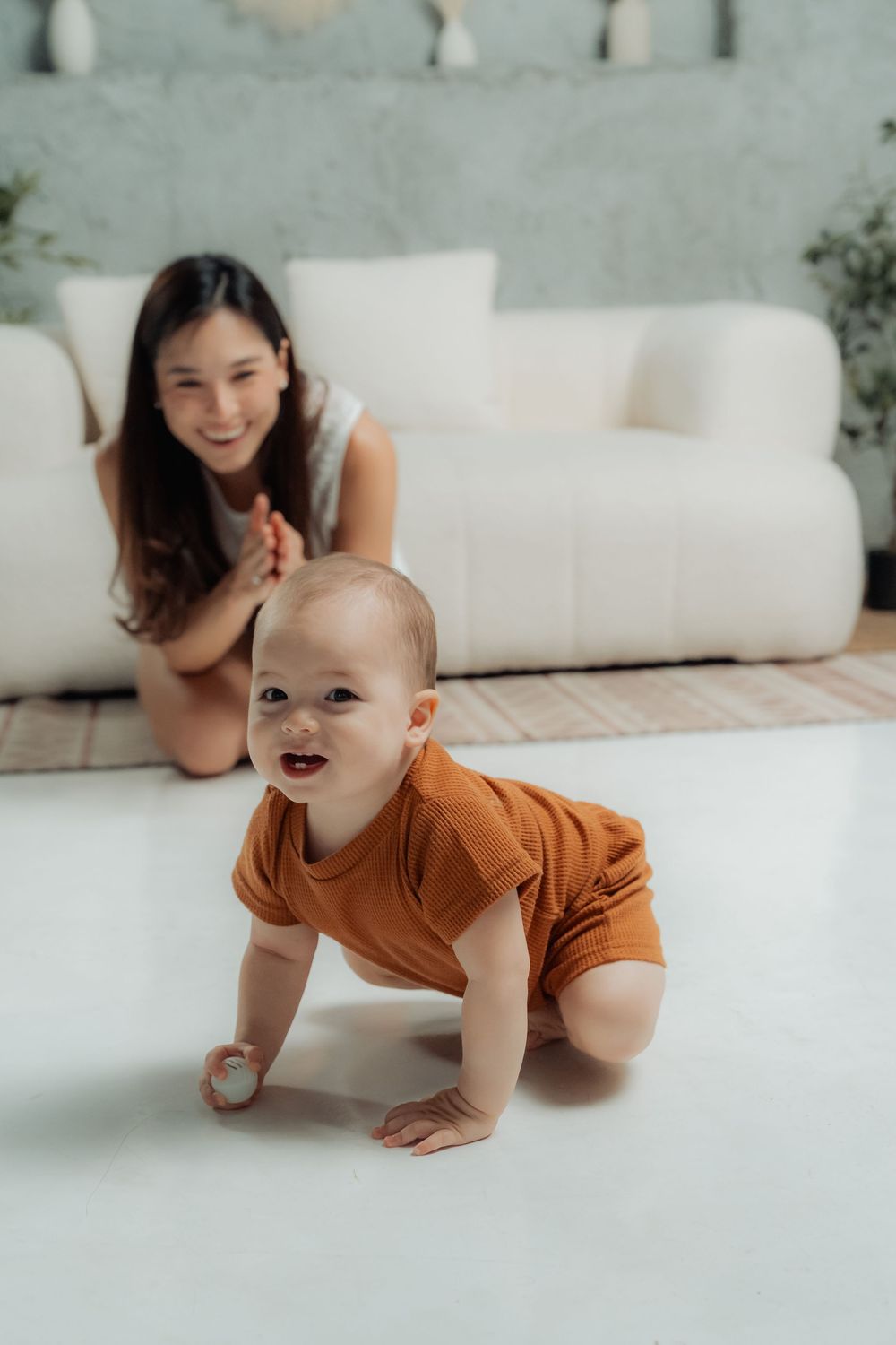 Baby in brown onesie crawling on white floor during indoor photoshoot.