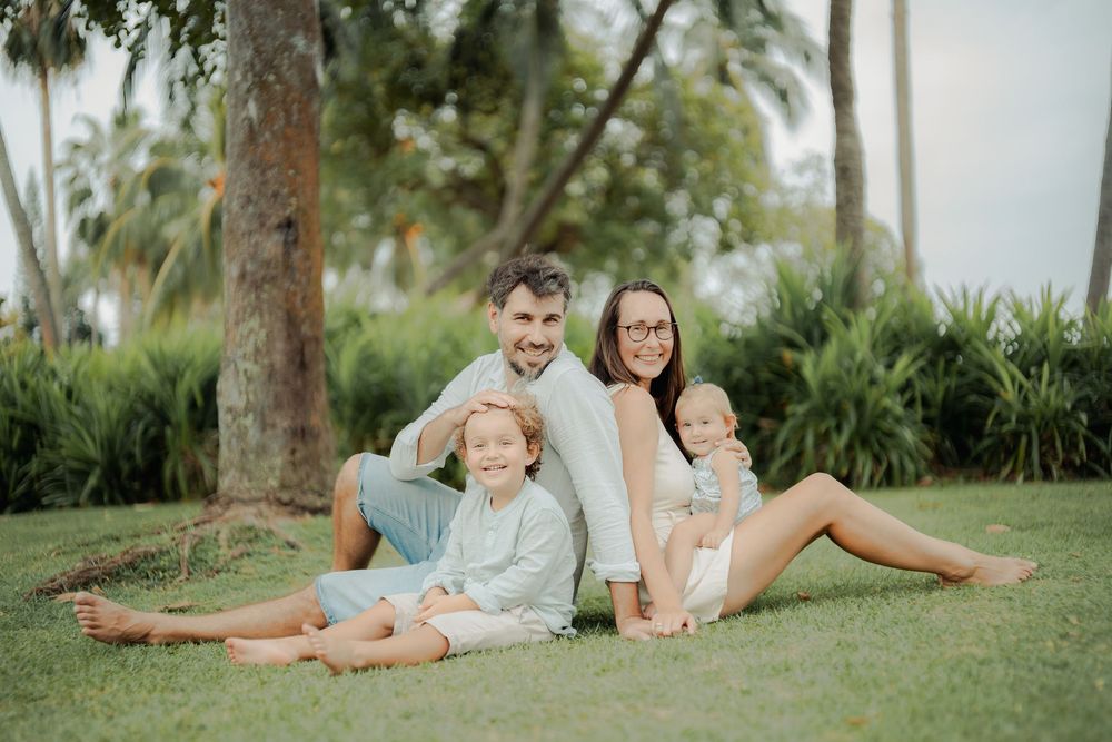 Family relaxing together on grass under palm trees during golden hour.