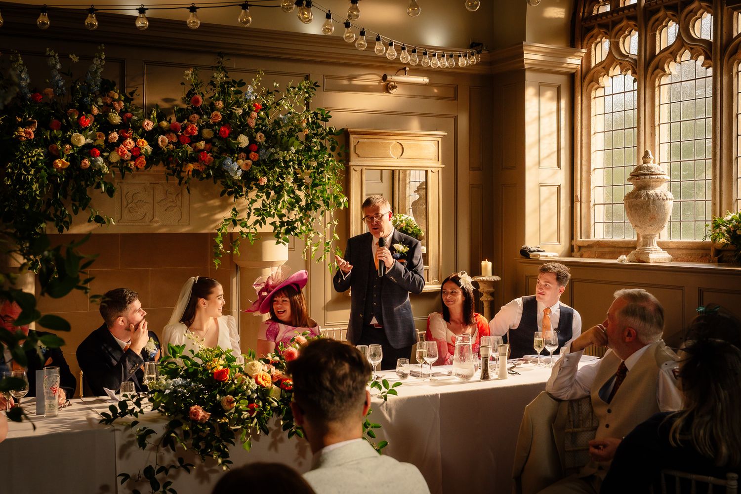 Wedding celebration in progress with guests seated at decorated tables under string lights. Ellingham Hall