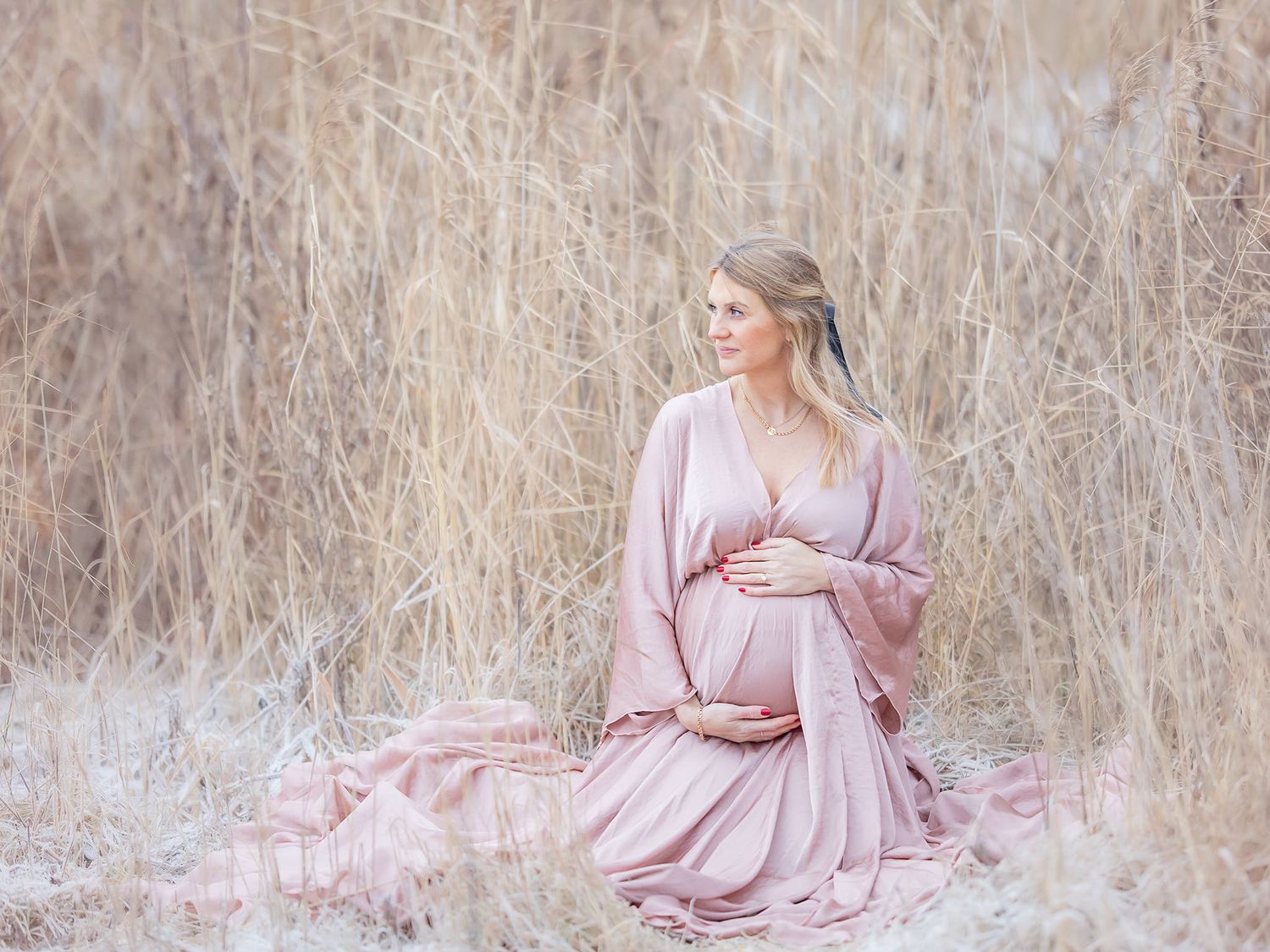 Gravid mamma i satinklänning, pastell gravidfotografering i västerås vid vass i snö. MemoriesbyM.se