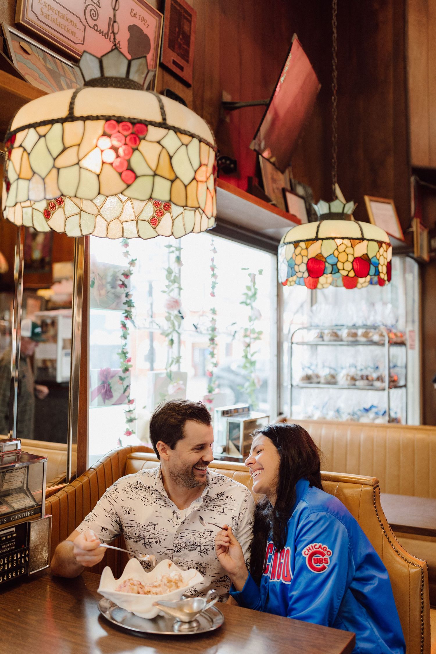 Romantic couple dining under vintage stained glass lamps in a cozy restaurant booth.